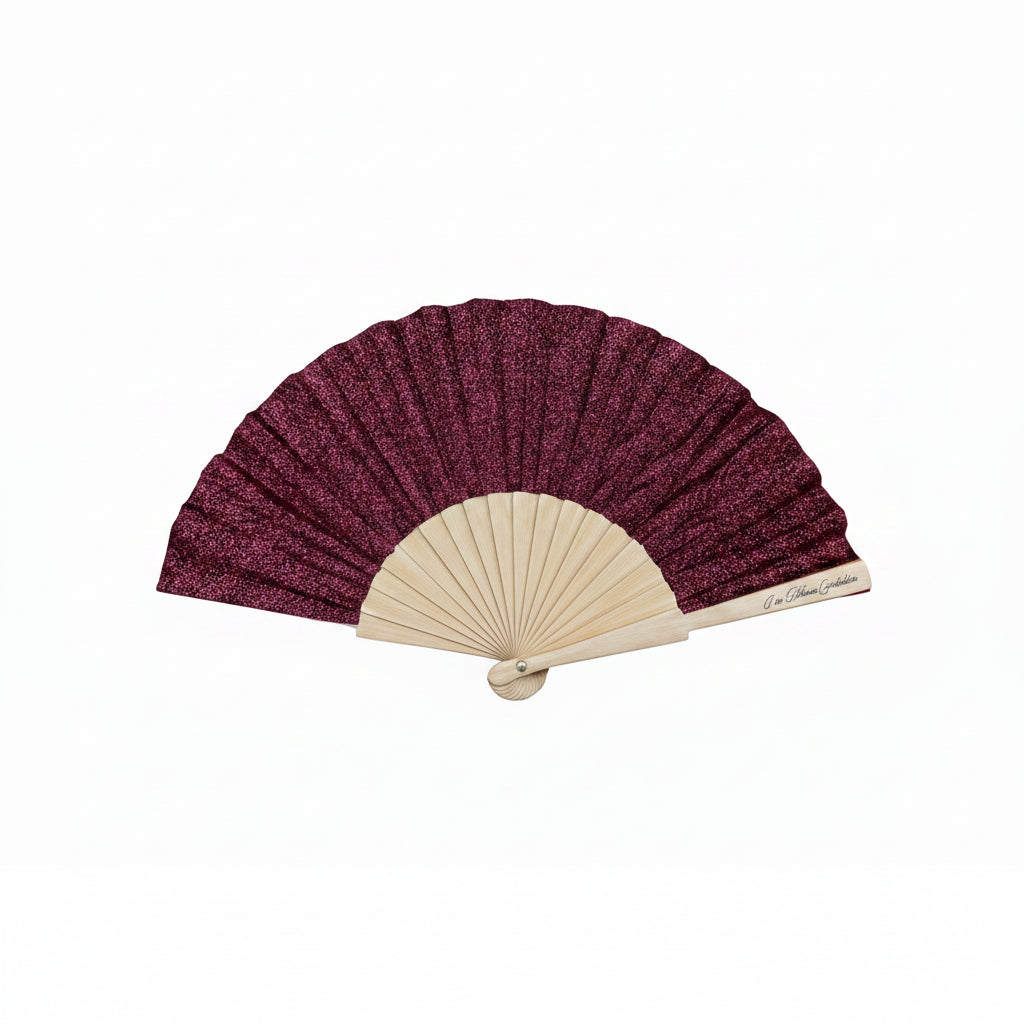 Handheld fan with deep pink glittery fabric and beige wooden frame on a gray stone surface