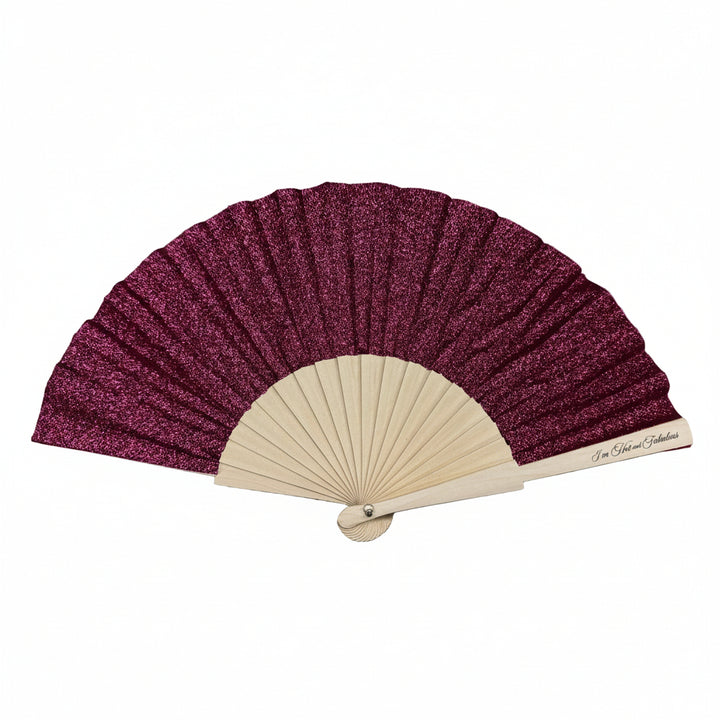 Handheld fan with purple glittery fabric and beige wooden frame on a gray stone surface
