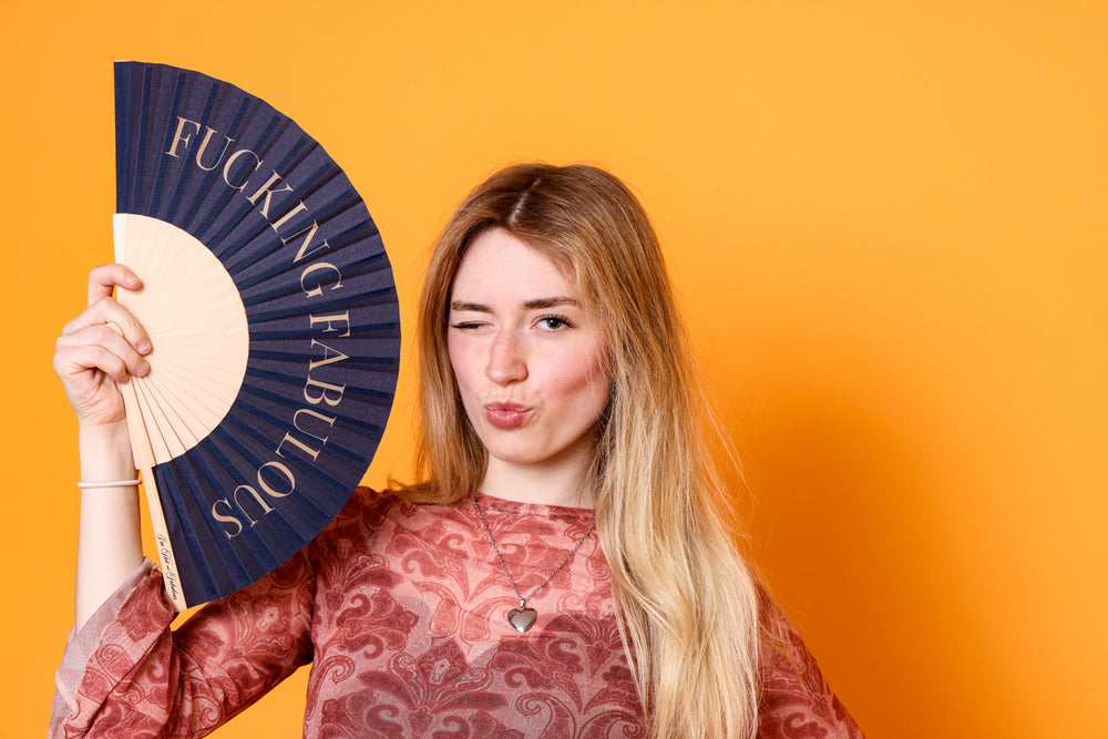 Woman holding a fan with 'Fucking Fabulous' text against an orange background