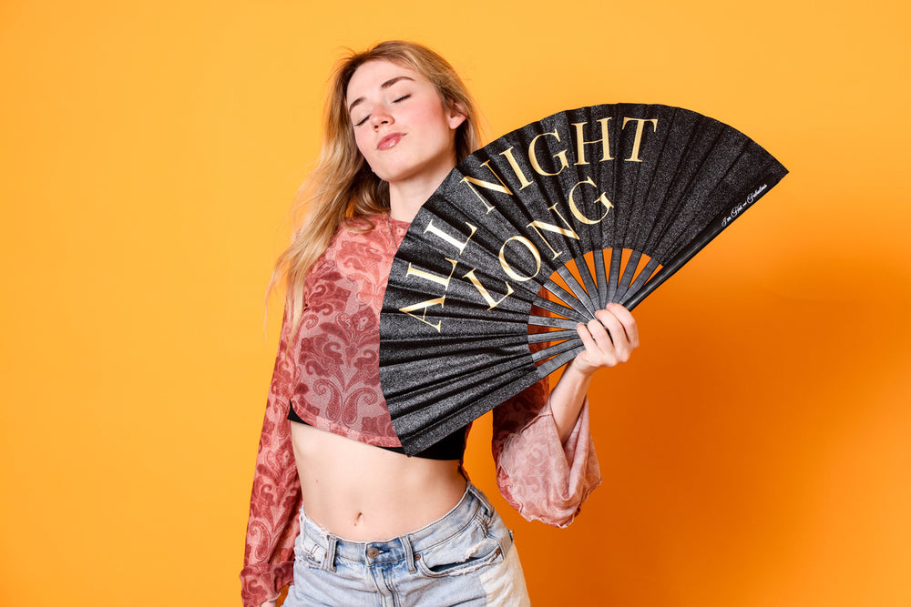 Woman holding a black fan with 'All Night Long' text against an orange background