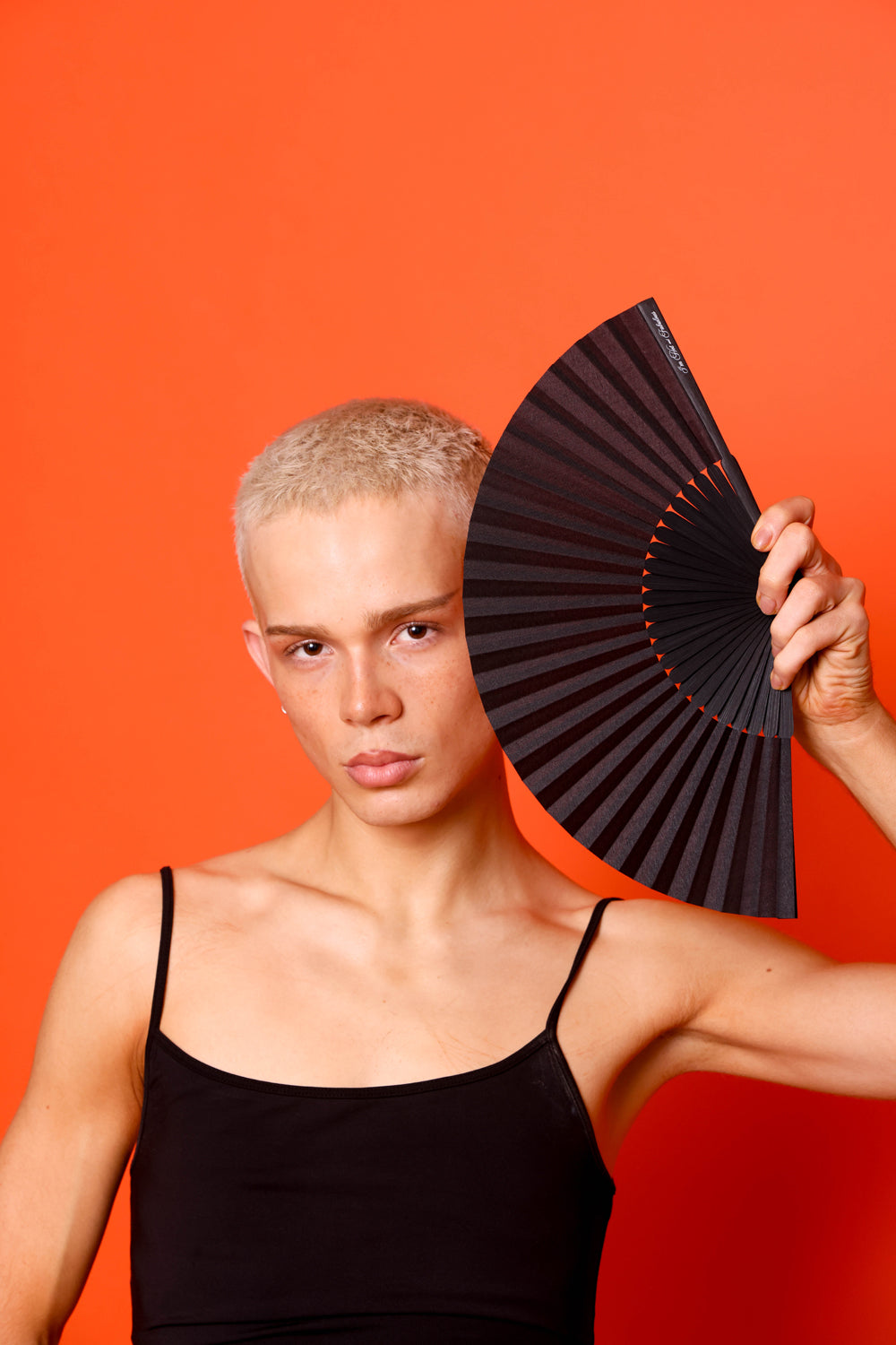 Person holding a black fan against an orange background