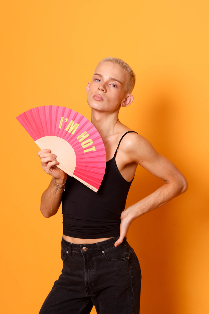 Person holding a pink fan with 'I'm hot' text against an orange background