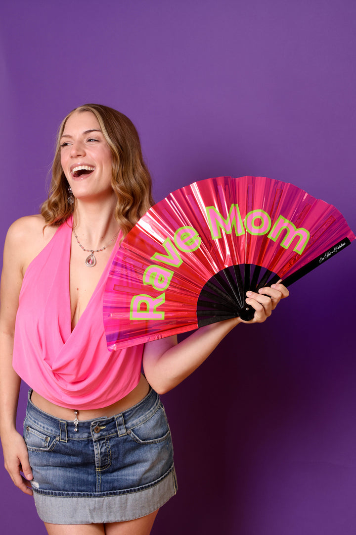 Woman holding a pink 'Rave Mom' fan against a purple background