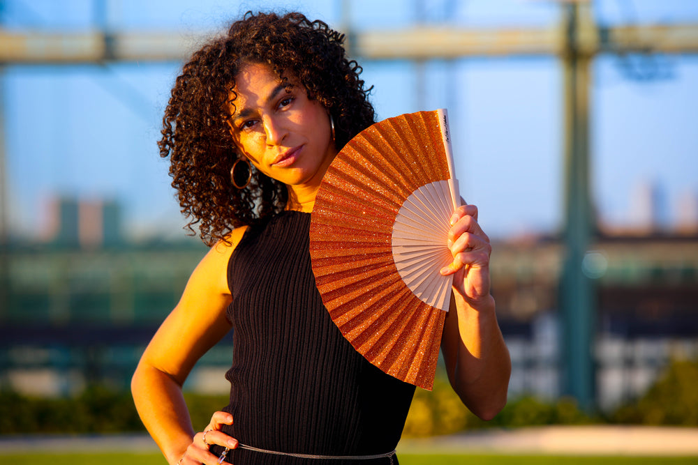 Woman holding a decorative orange fan outdoors with a blurred background