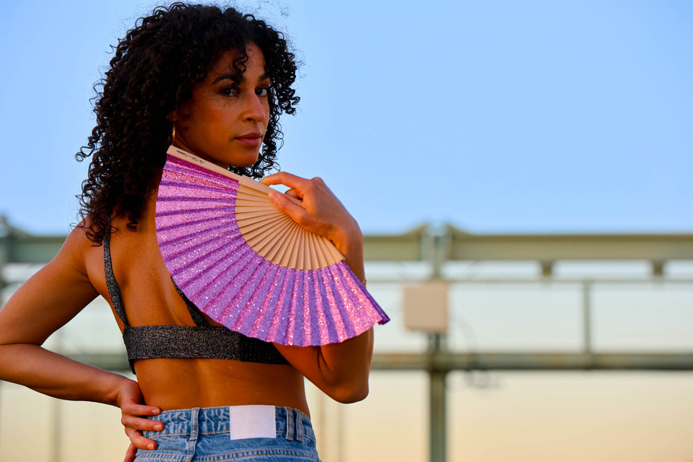 Woman holding a pink and gold fan against a clear blue sky