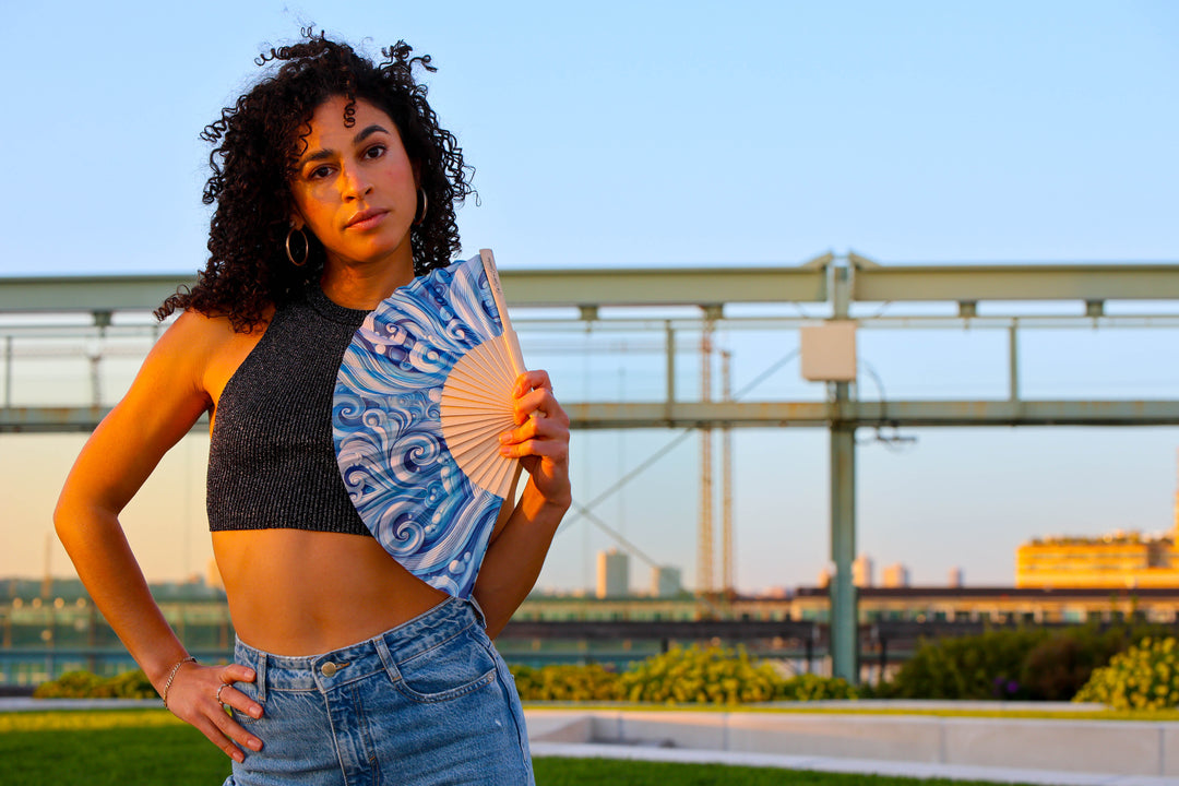 Woman holding a blue and white fan on a rooftop with a cityscape in the background