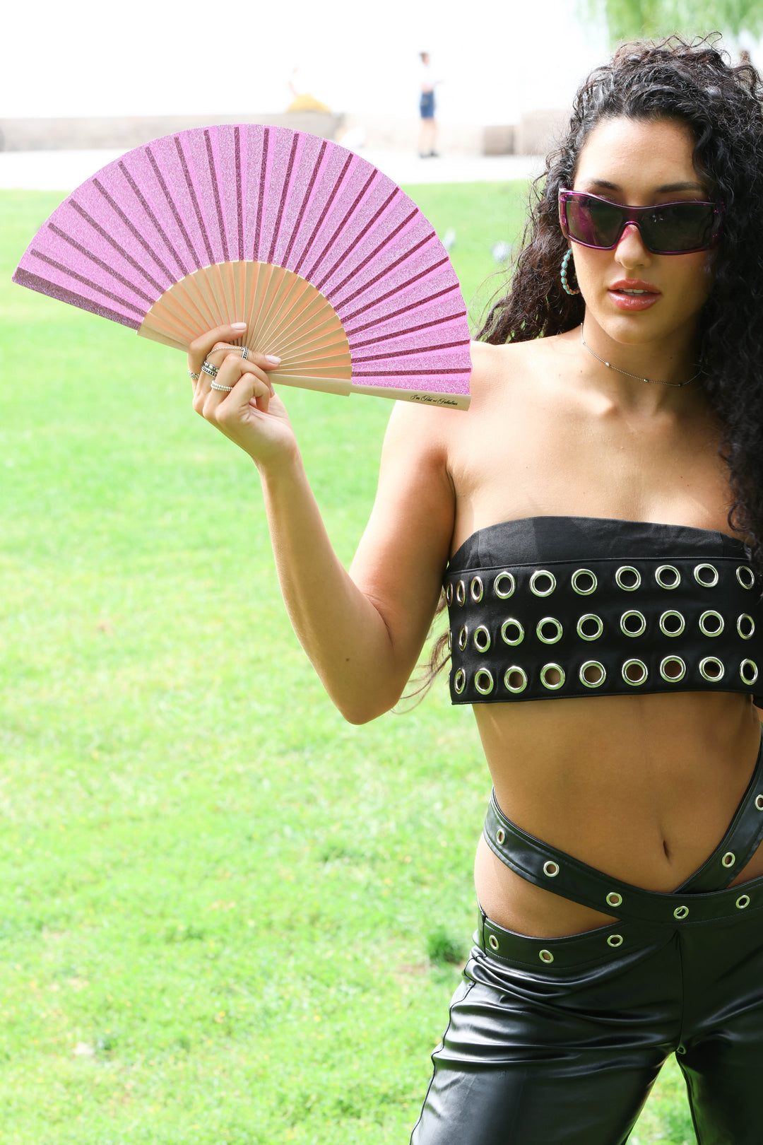 Woman holding a pink and wooden fan outdoors on a grassy background