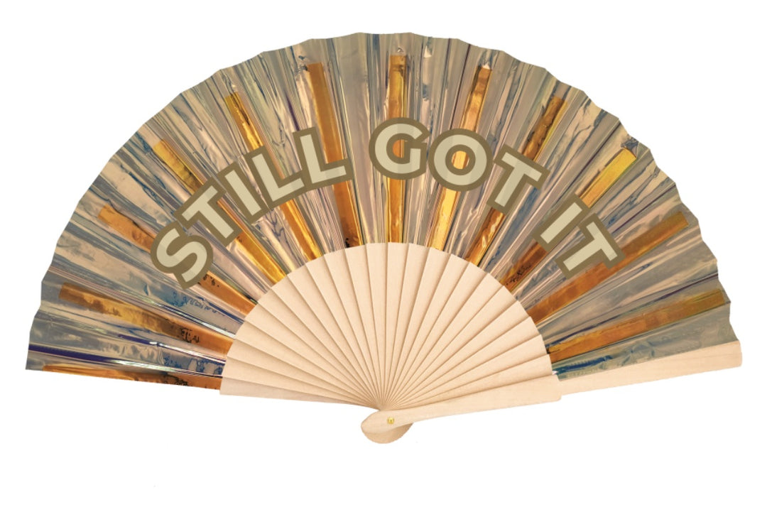 Custom gold holographic hand fan printed with STILL GOT IT in arched lettering on natural wood ribs
