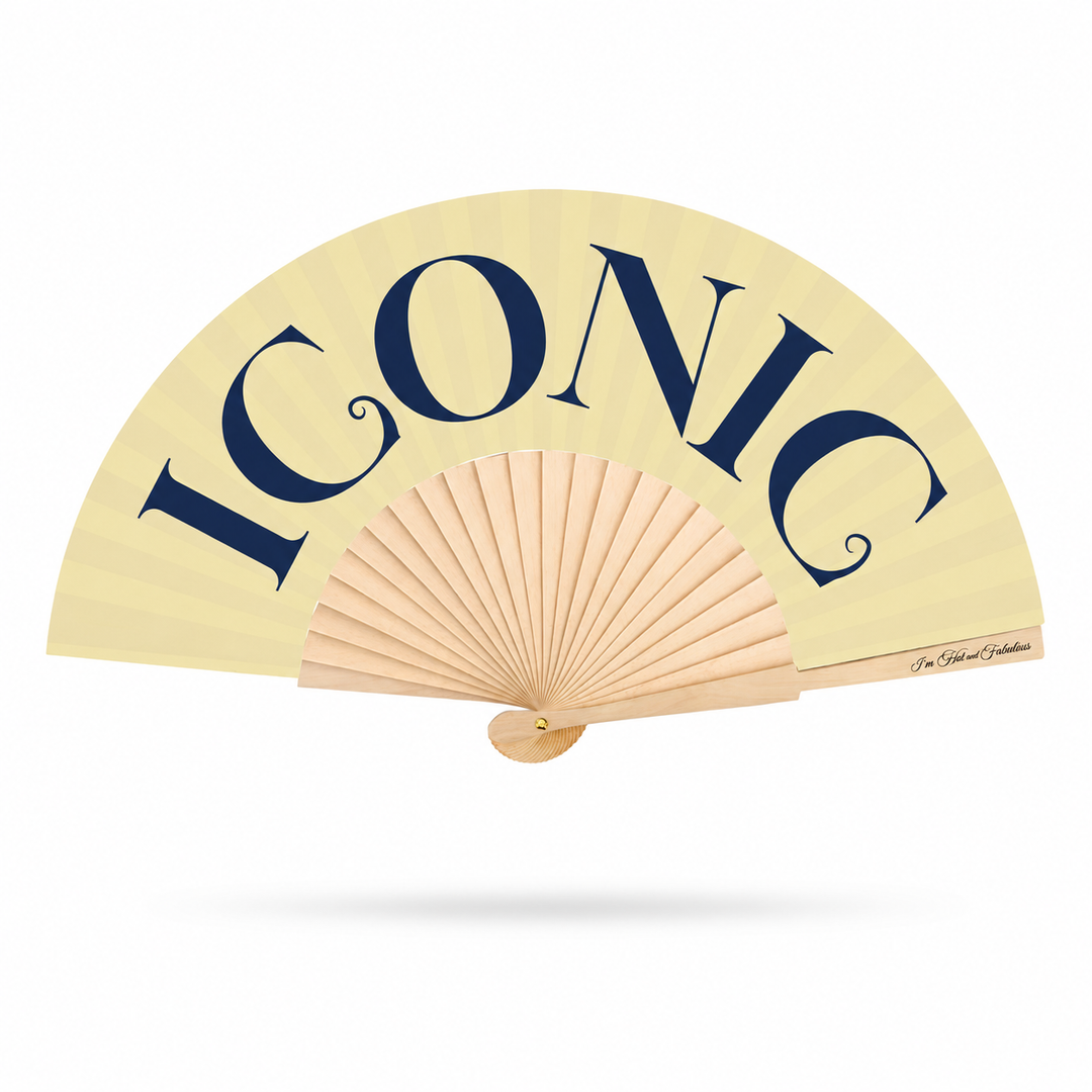 A folding hand fan with a cream-colored fabric canopy and natural wood ribs, featuring the word 'ICONIC' printed in large navy blue letters across the top. A small script signature is visible on the right edge of the canopy.