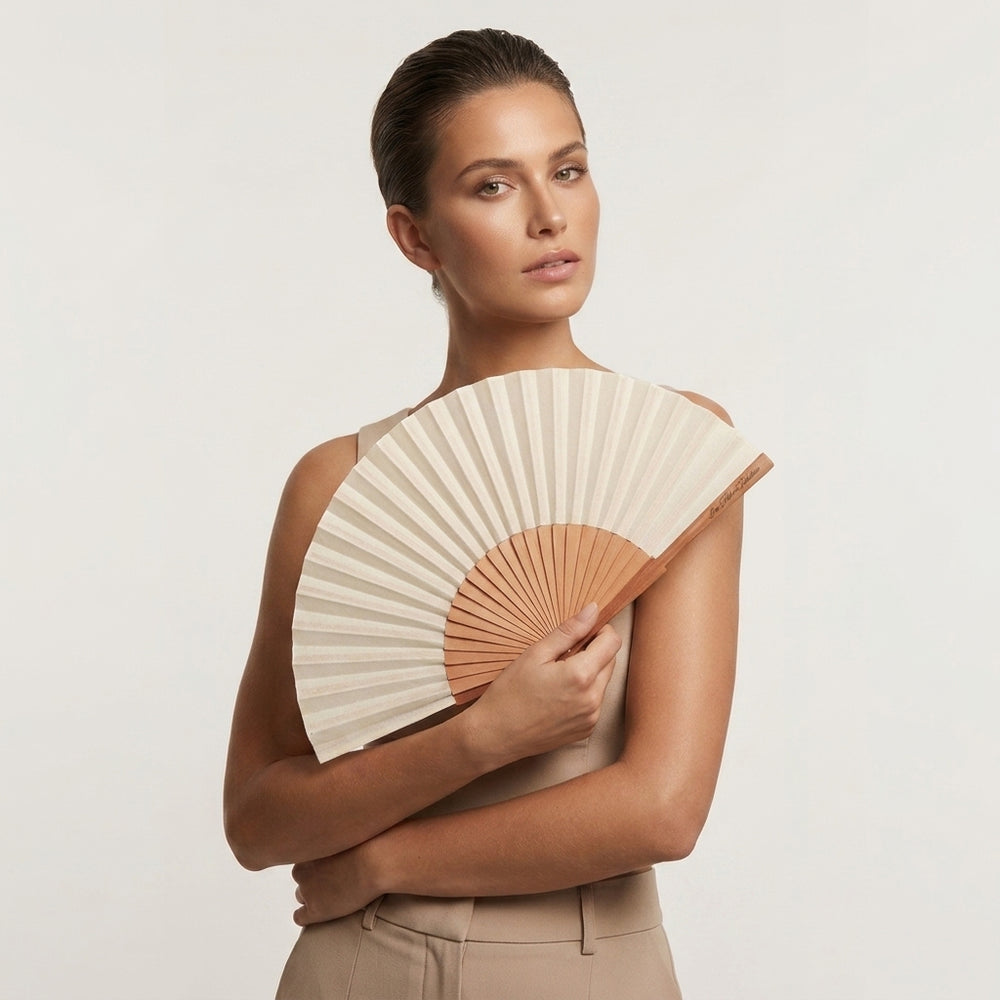 Woman holding a beige and brown fan against a plain background