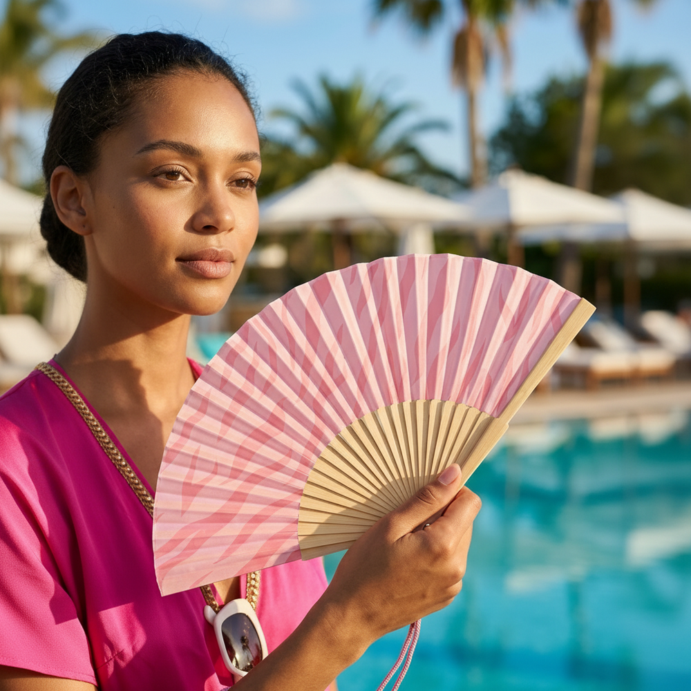 Woman holding a pink striped fan by a pool with palm trees in the background